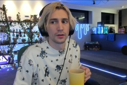 XQc, a streamer, sits holding a mug of coffee at his desk.